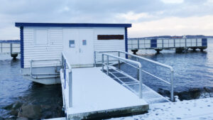 Gebäude am Wasser mit Schnee bedeckt. Im Hintergrund der Badesteg