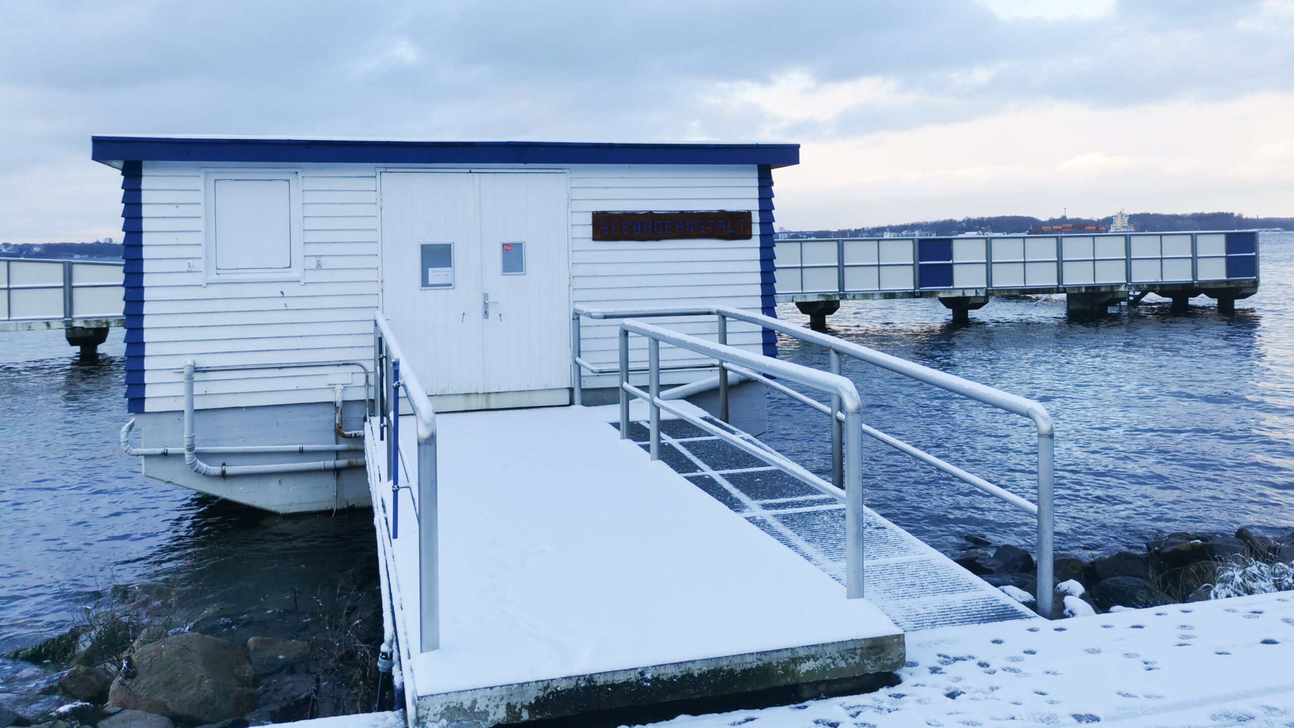 Gebäude am Wasser mit Schnee bedeckt. Im Hintergrund der Badesteg