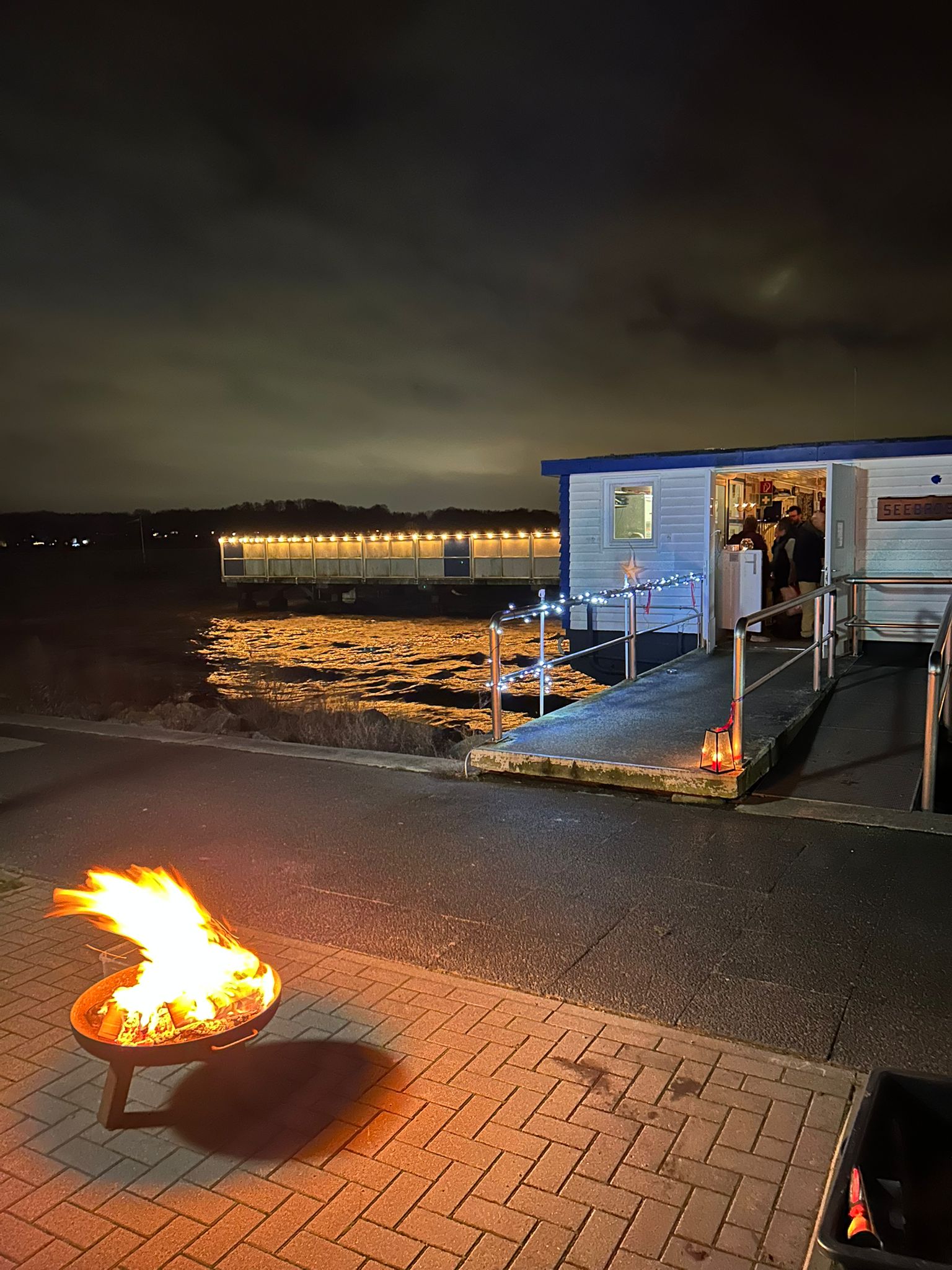 Gebäude am Abend im Dunklen am Wasser mit Feuerschale